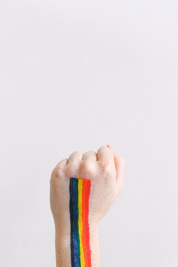 A hand with rainbow body paint raised in a prideful gesture on a white background.